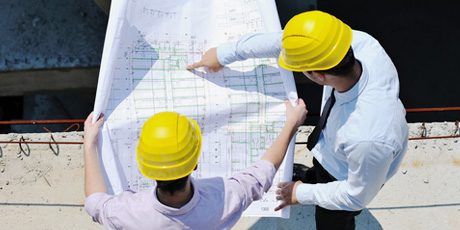 Zwei Bauleiter mit Schutzhelmen studieren einen Plan auf der Baustelle